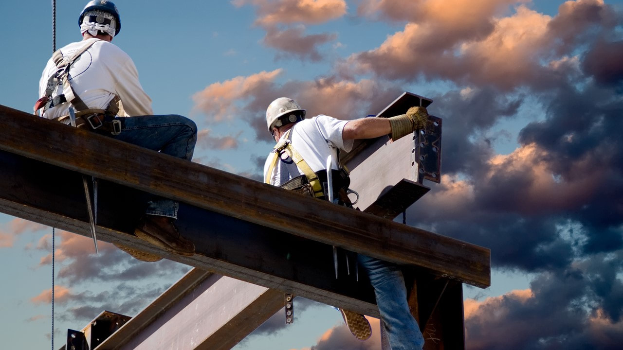 2 men sitting on top of beams, erecting a metal building - TWFG Tony Voiron - Commercial Insurance 